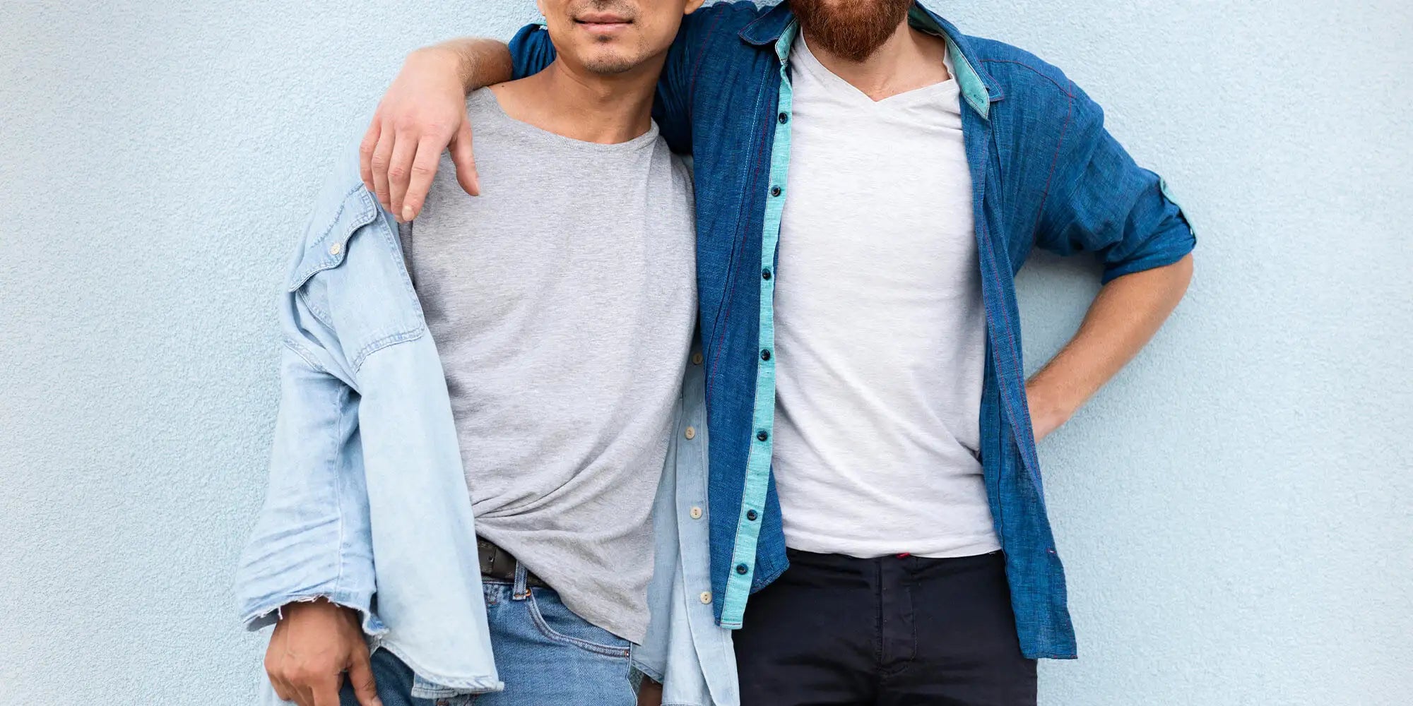 Banner für die Kategorie „Herren Neuheiten“ im Boxxers Online Shop. Zwei Männer stehen locker Arm in Arm nebeneinander und tragen lässige Outfits aus T-Shirts und offenen Jeanshemden vor einer hellblauen Wand.