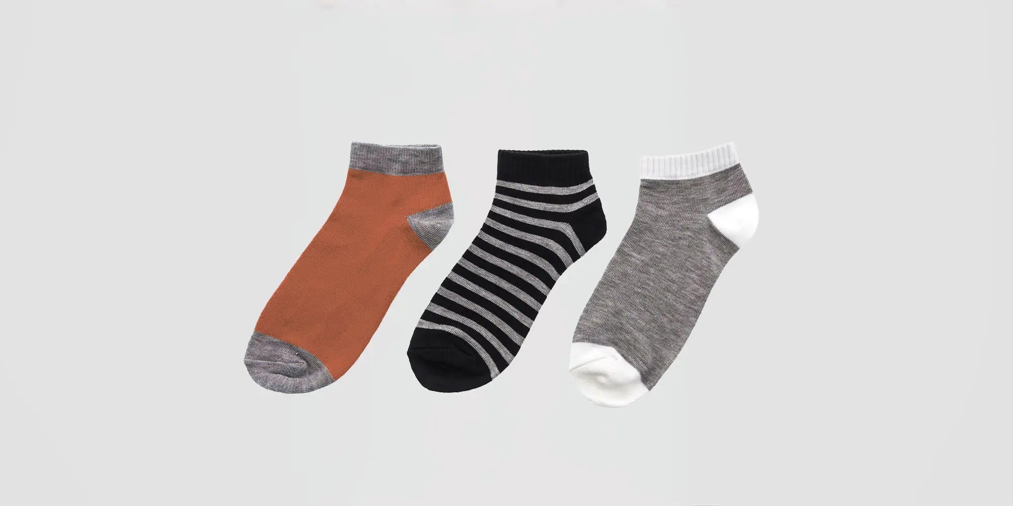 Banner für die Kategorie „Herren Sneakersocken & Füsslinge“ im Boxxers Online Shop. Drei kurze Männersocken in Braun, Schwarz-Weiß gestreift und Grau-Weiß liegen nebeneinander vor einem hellgrauen Hintergrund.