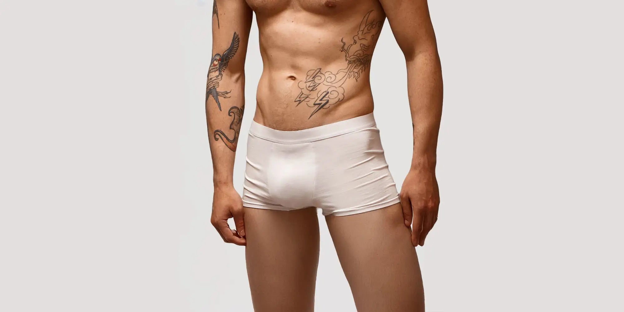 Banner für die Kategorie „Herren Trunks“ im Boxxers Online Shop. Ein Mann trägt enganliegende, weiße Trunks und steht vor einem hellgrauen Hintergrund.