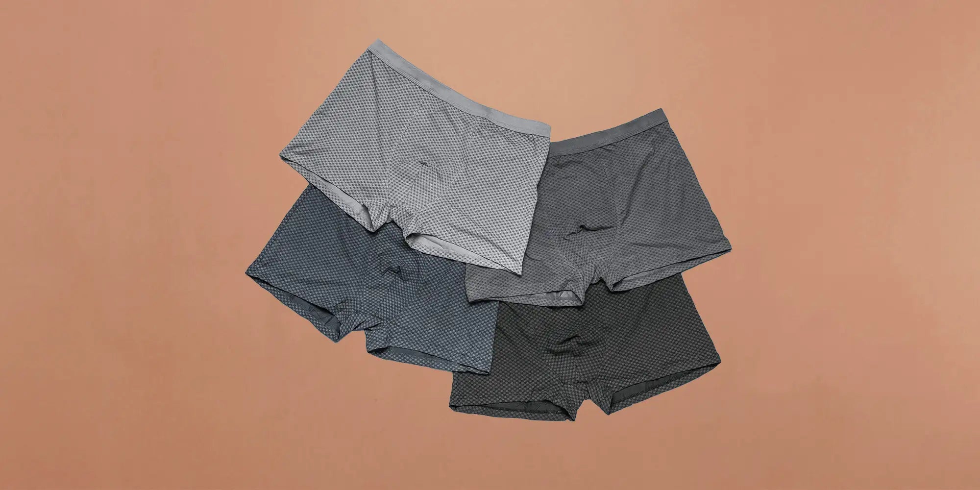 Banner für die Kategorie „Herren Unterwäsche Sets“ im Boxxers Online Shop. Vier gemusterte Herren-Boxershorts in verschiedenen Grautönen liegen leicht überlappend vor einem beigefarbenen Hintergrund.